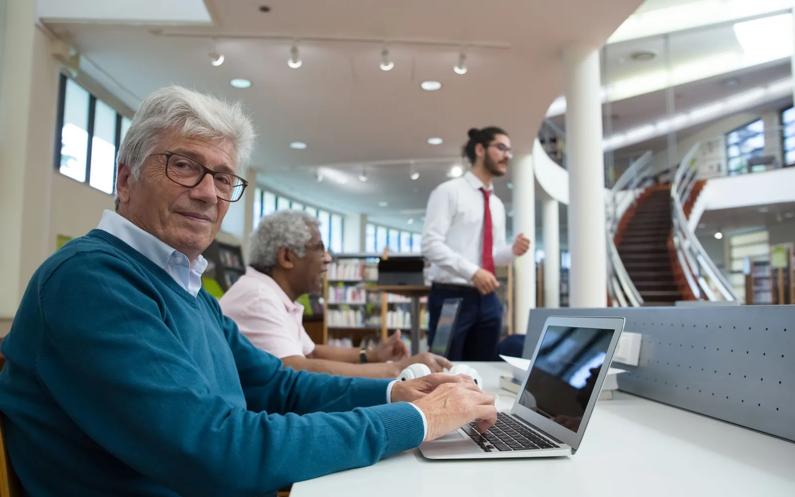 Older adults using laptops together in a public library learning space